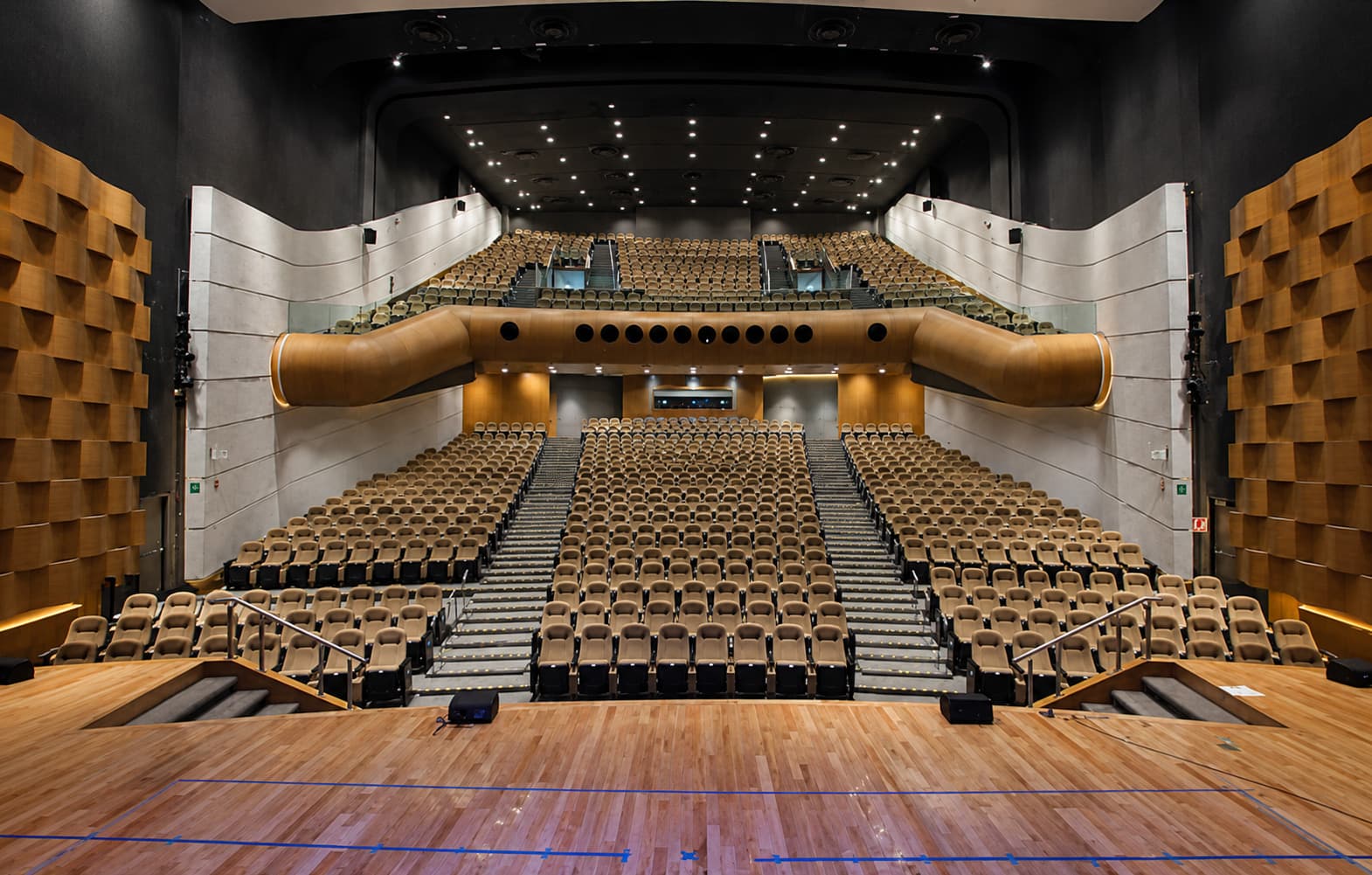 Sala del auditorio vista desde el escenario, con butacas, palco de madera y paneles acústicos