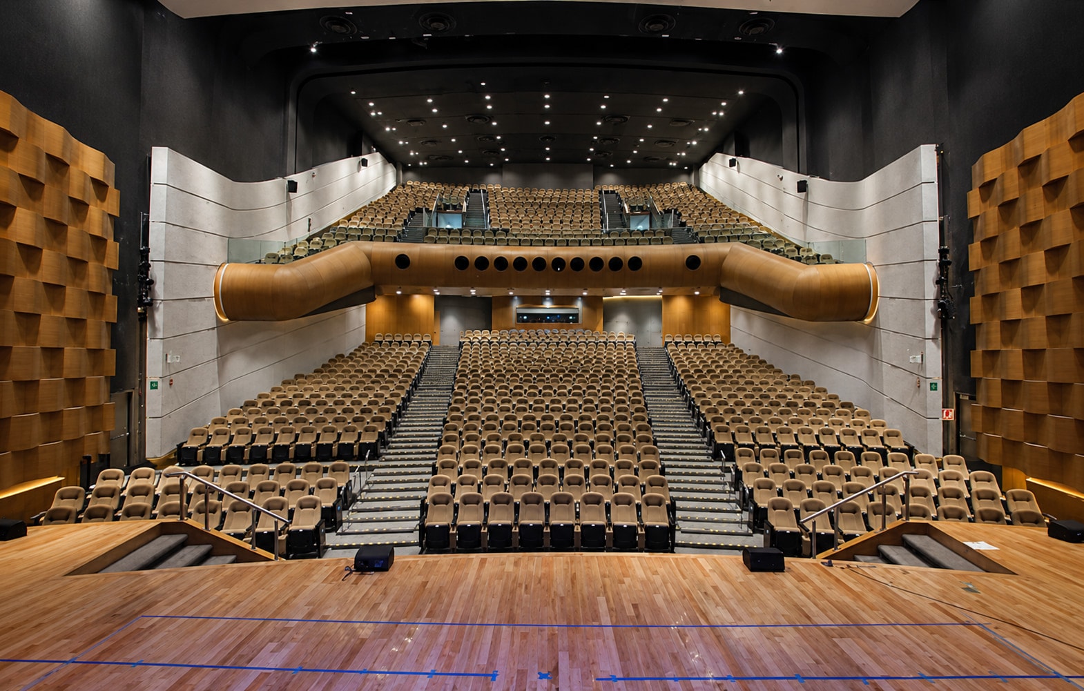 Sala del auditorio vista desde el escenario, con butacas, palco de madera y paneles acústicos